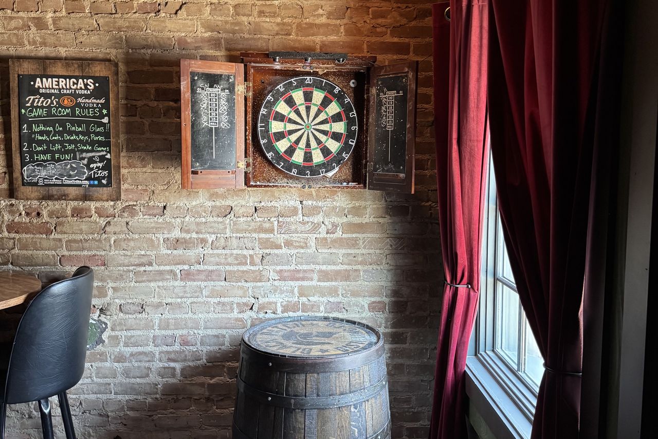 The dartboard in its wooden cabinet on the brick wall, house rules chalked beside it